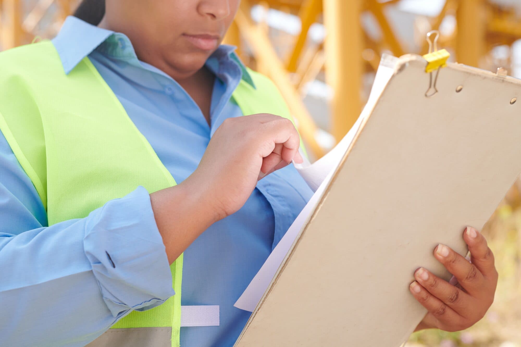 An engineer in safety gear reviewing project documents on a clipboard at a construction site