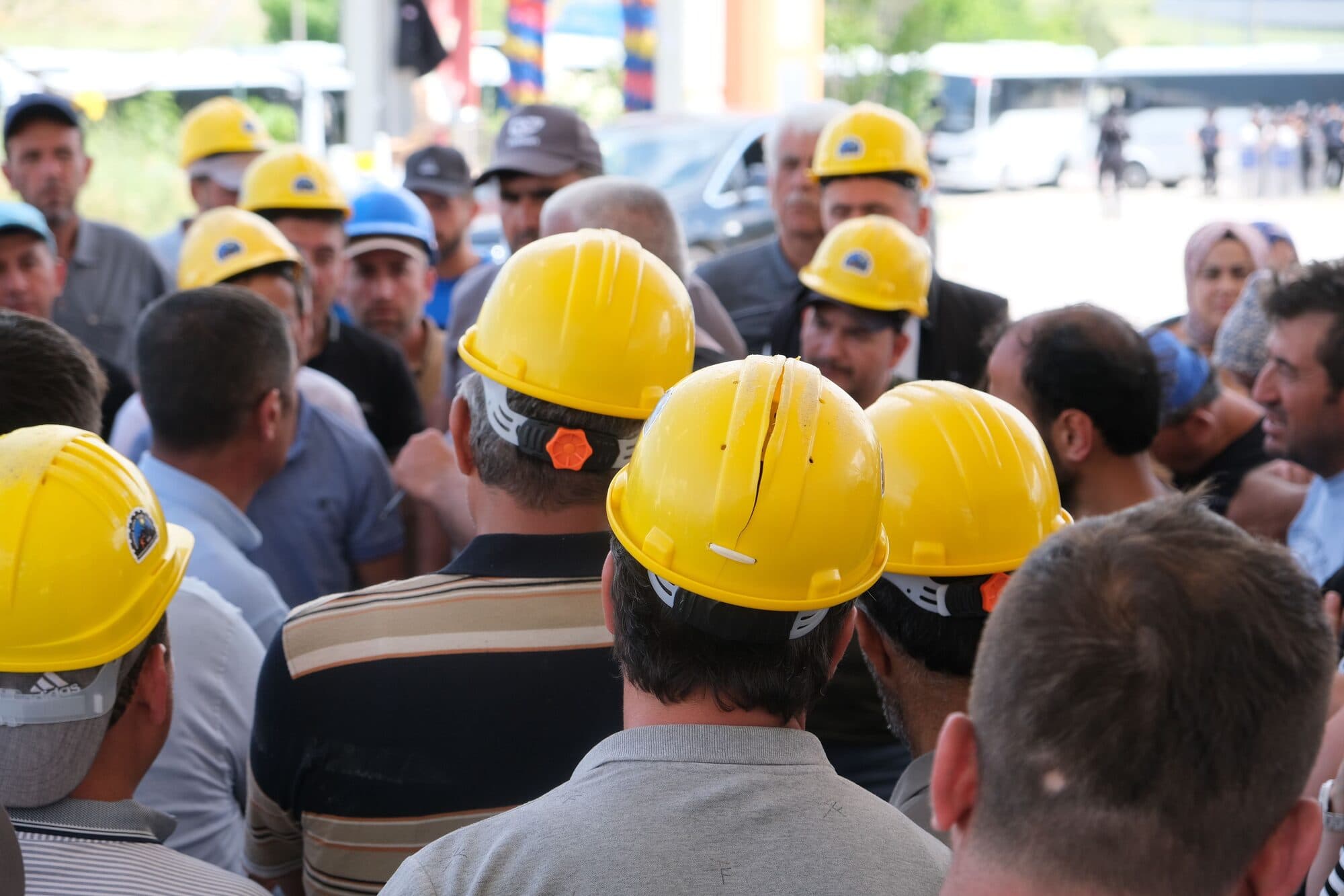 A gathering of construction workers wearing yellow hard hats, engaged in discussion outdoors.